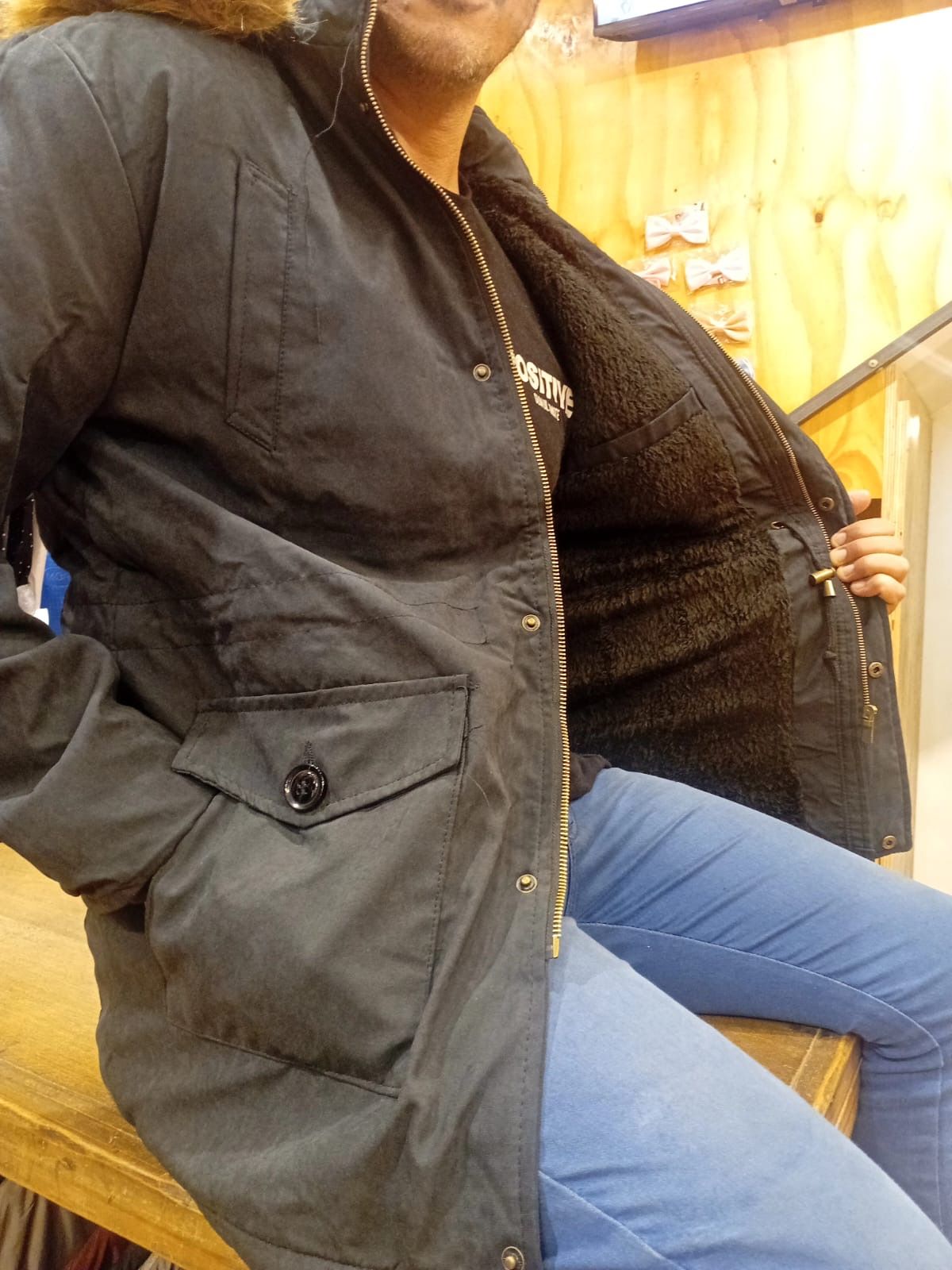 Una mujer que lleva una chaqueta negra y jeans azules está sentada en una mesa.