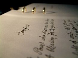 Close-up of a handwritten ring-bound notebook page with cursive notes and metal rings, softly lit.