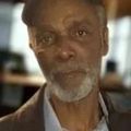 Close-up of a man with a gray beard, looking at the camera indoors