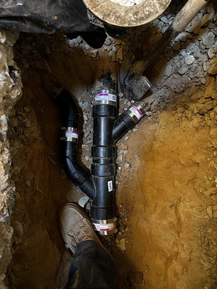Black PVC pipes installed in a dirt trench, forming a Y-shaped plumbing junction