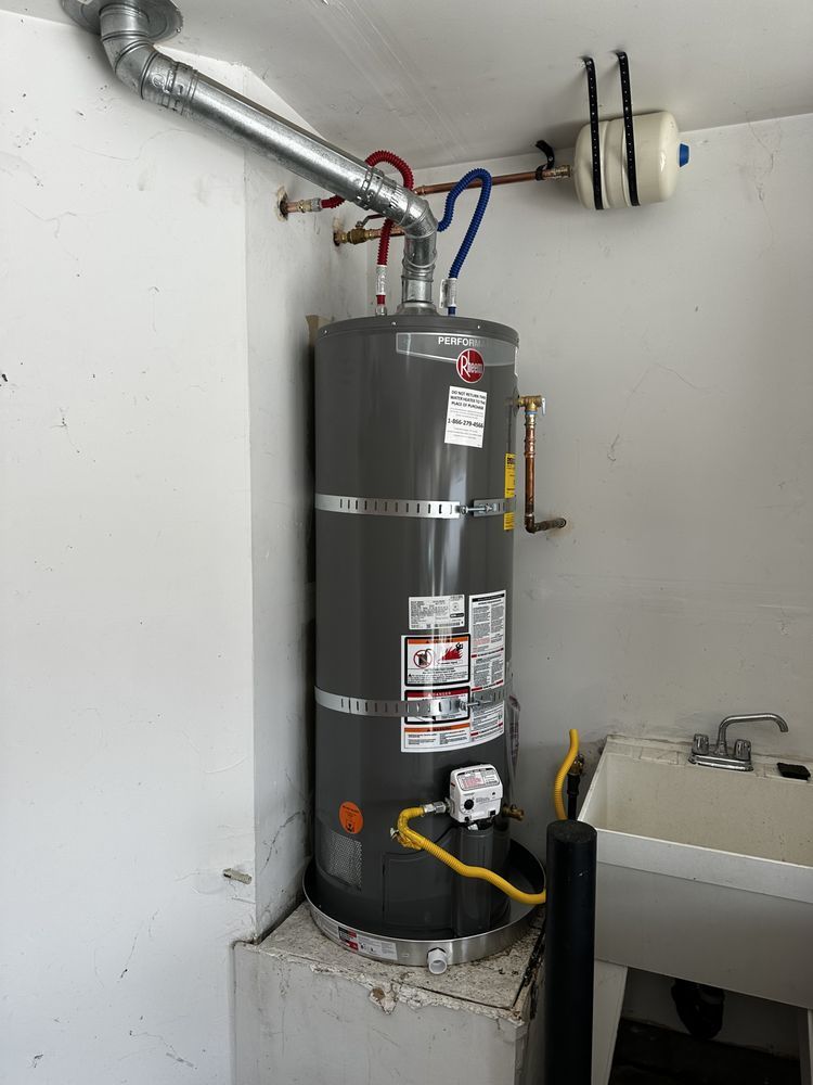 Water heater in a utility closet with exposed pipes, wiring, and an adjacent sink