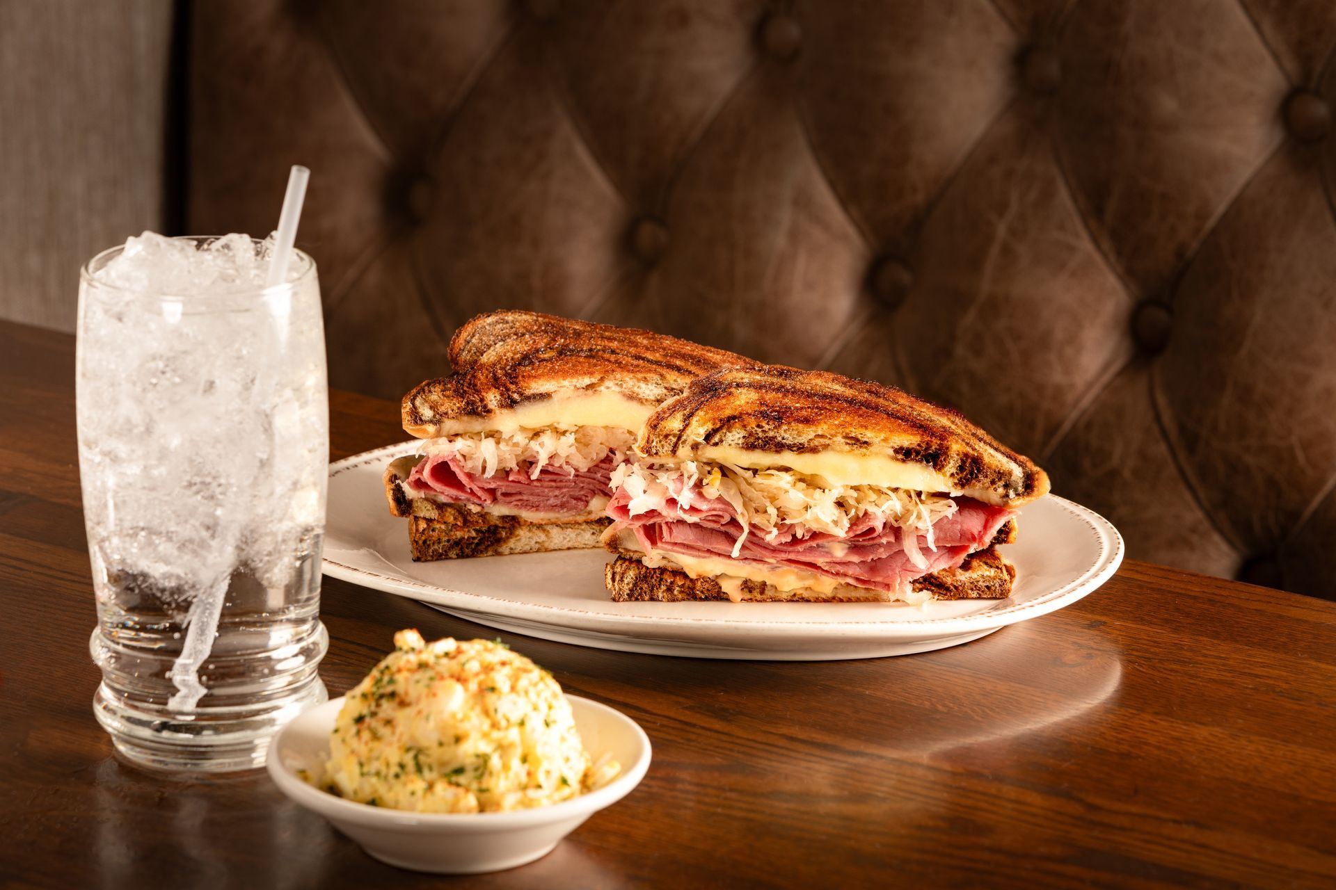 Reuben sandwich with potato salad and a glass of ice water on a table in a restaurant.