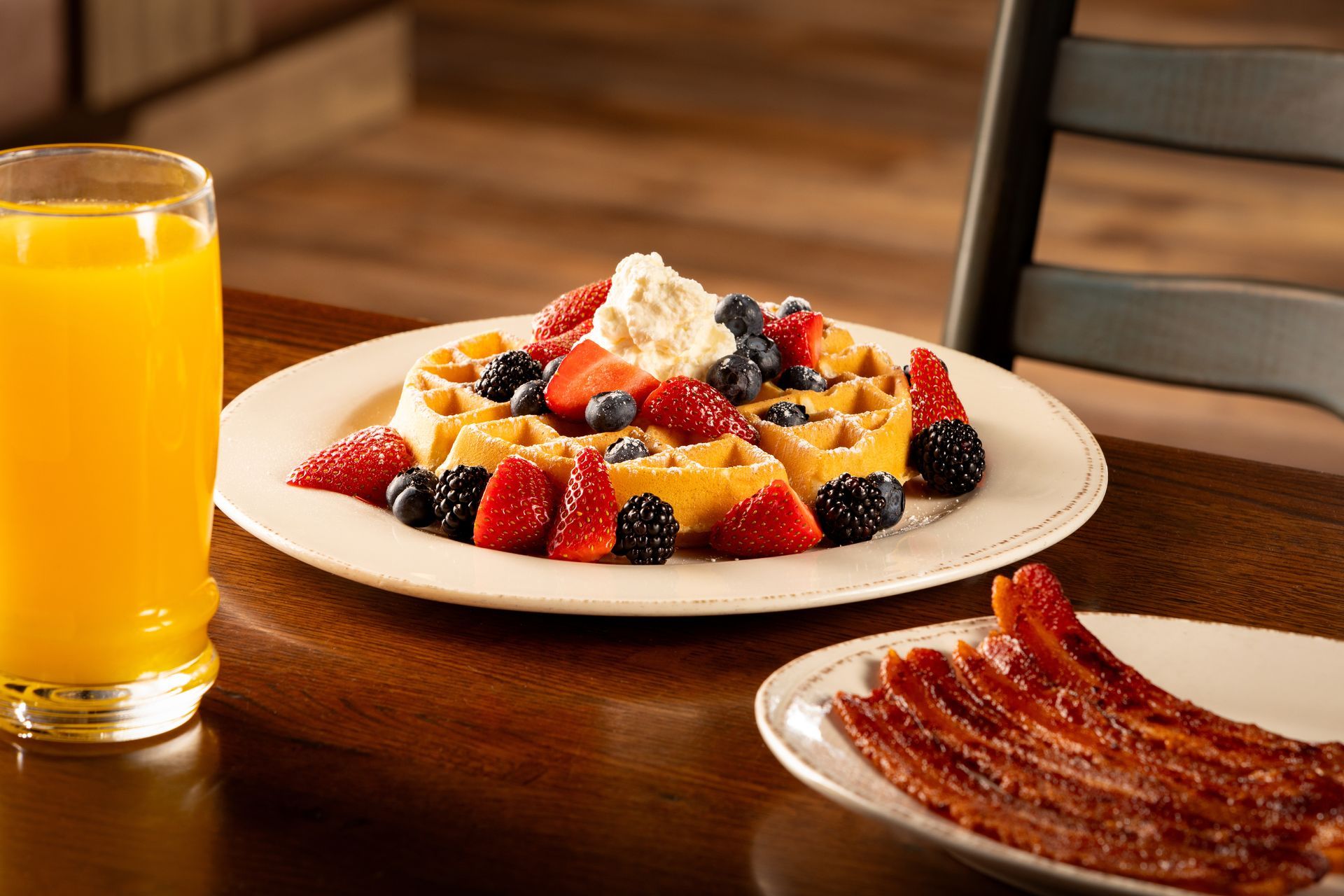 Plate of waffles topped with berries and whipped cream, bacon, and a glass of orange juice.