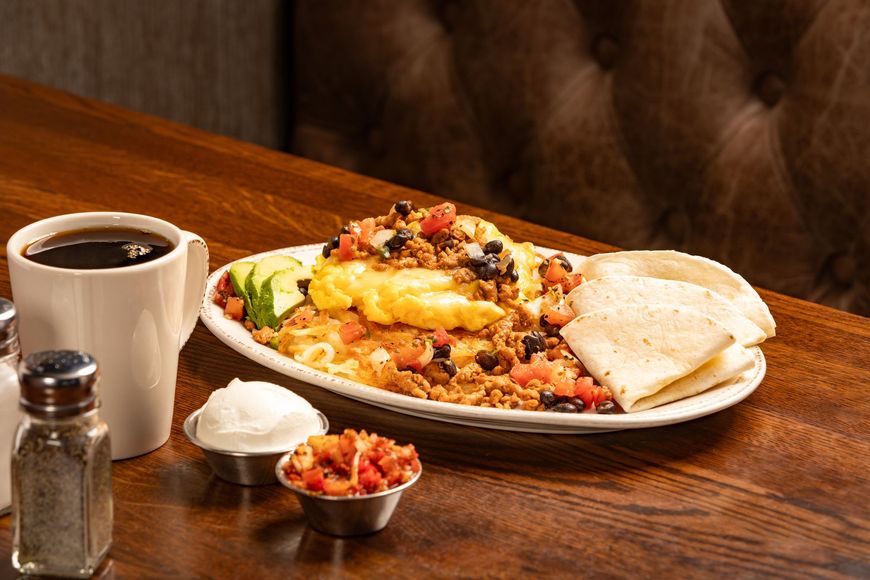 Breakfast plate with eggs, beans, and tortillas; served with coffee, sour cream, and salsa.