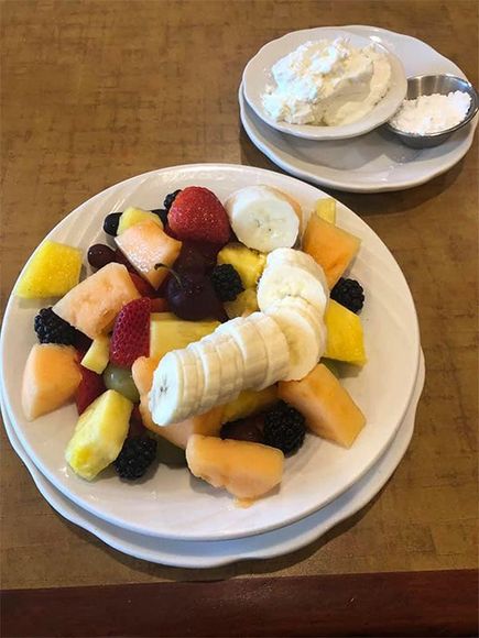 Plate of fruit salad with whipped cream and sugar on a side plate.