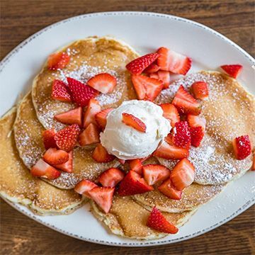 Pancakes topped with sliced strawberries and a scoop of whipped cream on a white plate.