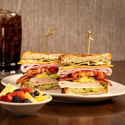 Club sandwiches on a plate, with a bowl of fruit and a glass of cola.