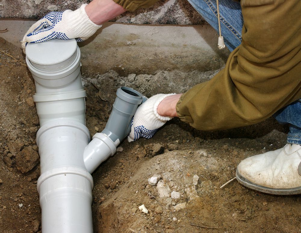 Person in Gloves Connecting Gray Pipe to White Drain Pipes in a Trench — No. 2 Plumbing In Indooroopilly, QLD