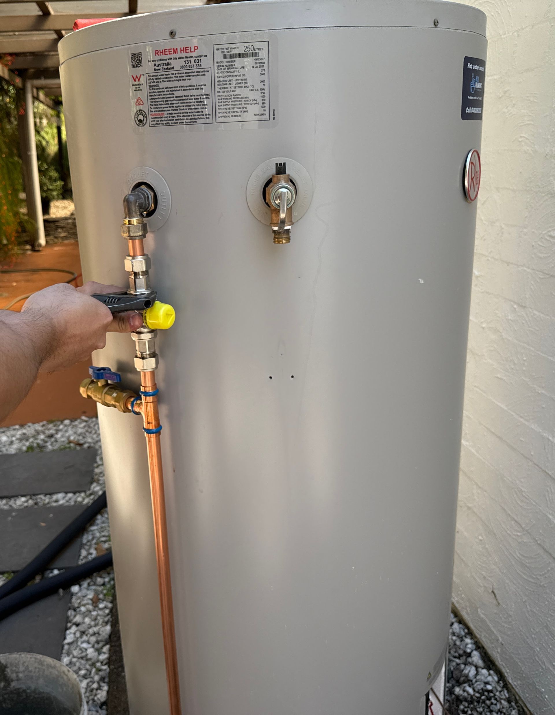 Person turns a valve on a copper pipe connected to a grey water heater outside. — No. 2 Plumbing In Kenmore, QLD