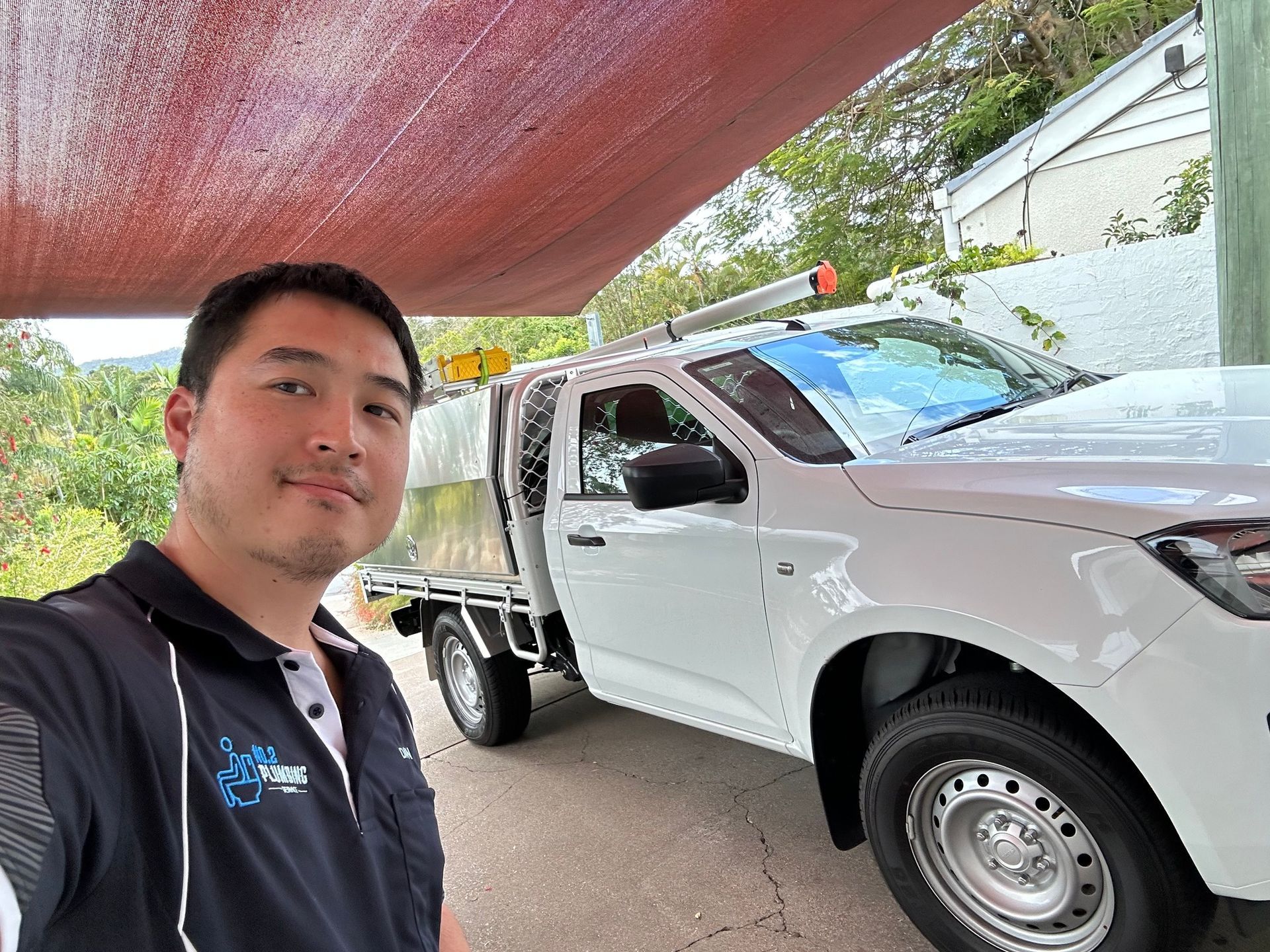 Man stands next to a white pickup truck, under a red awning, outdoors.