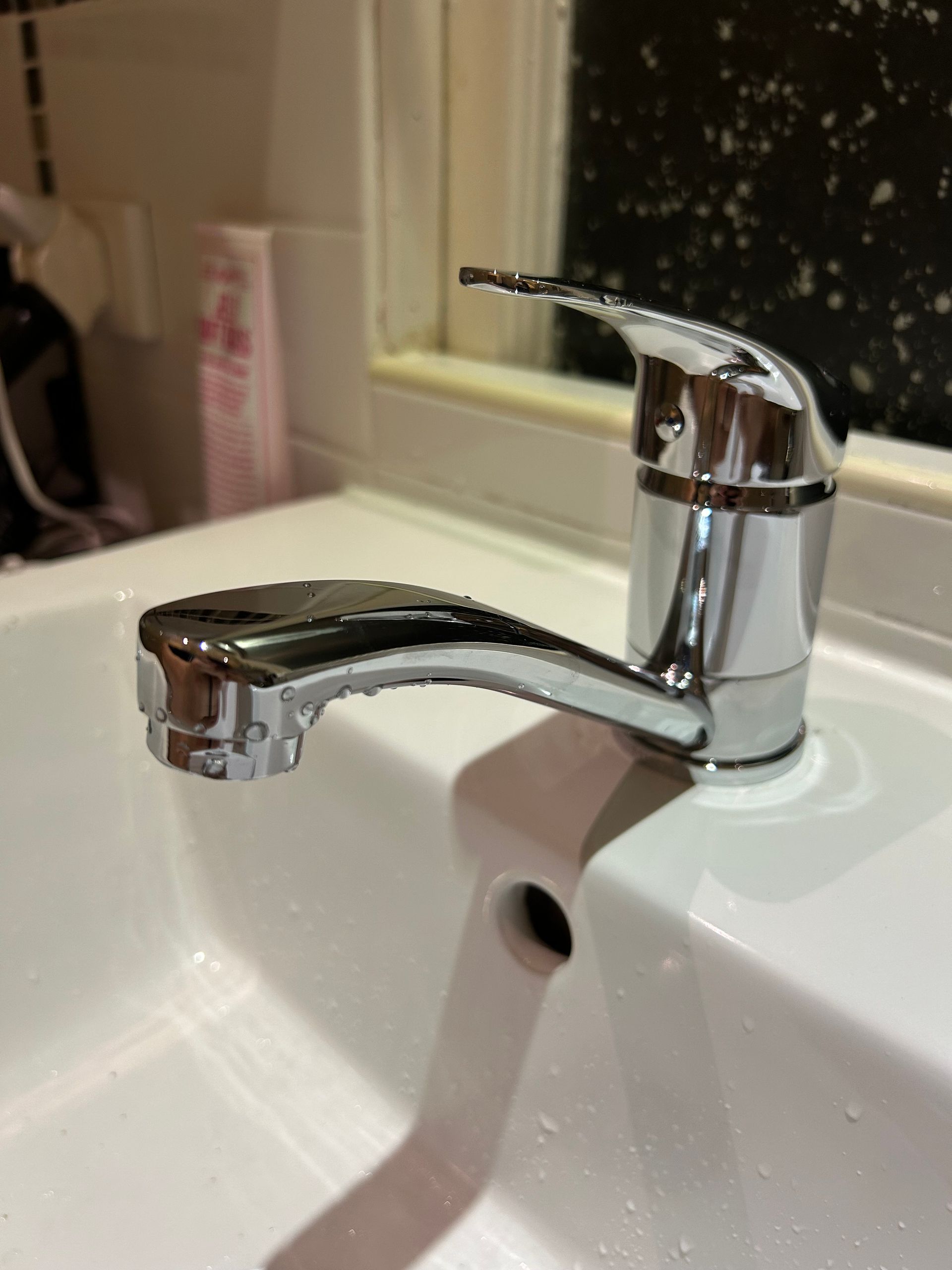 A close-up of a modern chrome bathroom faucet with water droplets, mounted on a white porcelain sink — No. 2 Plumbing In Toowong, QLD