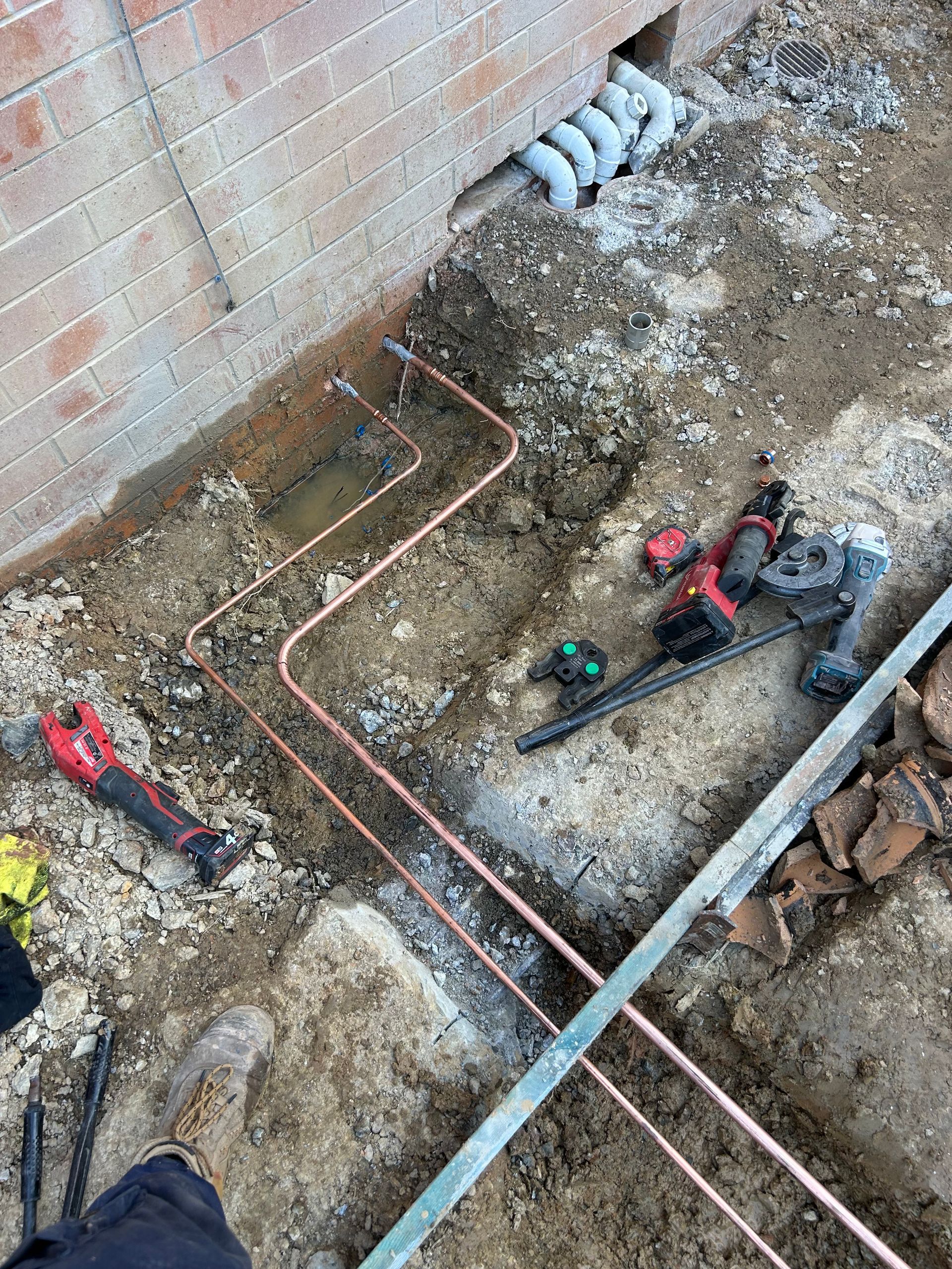 Copper Plumbing Pipes Installed in a Dirt Trench Beside a Brick Wall — No. 2 Plumbing In Kenmore, QLD