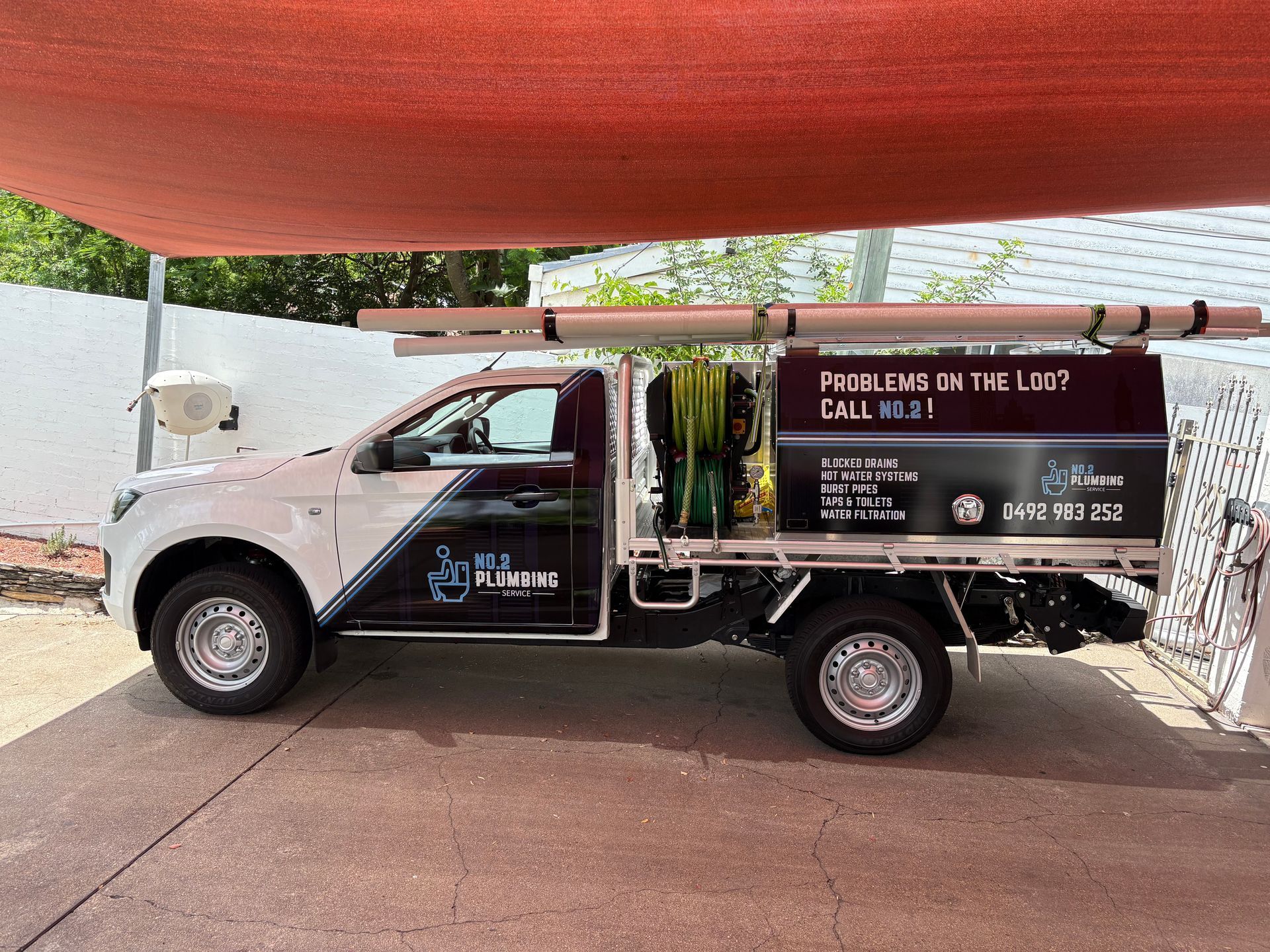 A white and black plumbing service utility truck parked outdoors under a shade sail, displaying business branding — No. 2 Plumbing in Kenmore, QLD