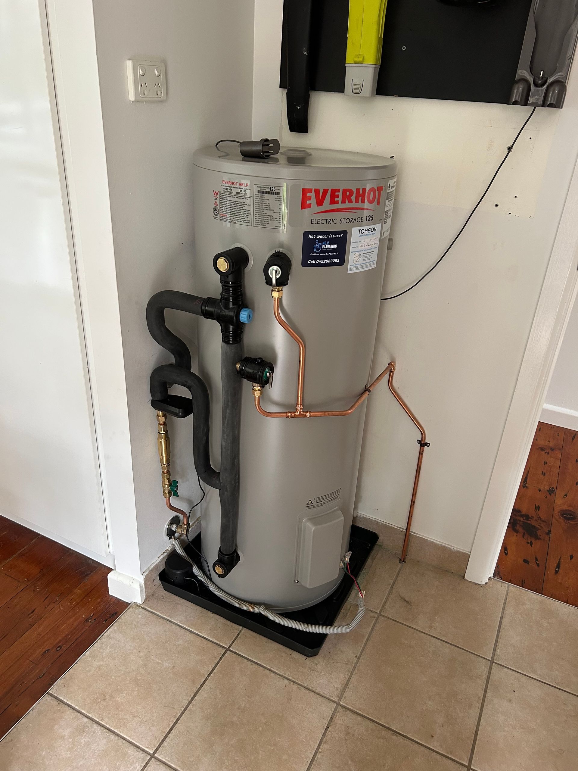 A grey cylindrical outdoor water heater unit positioned against a brick wall on gravel ground — No. 2 Plumbing In Kenmore, QLD