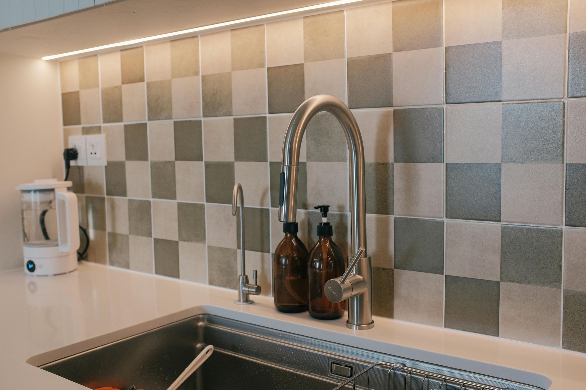 A Person Uses Pliers and a Wrench to Repair Plumbing Under a White Sink on a Tiled Floor — No. 2 Plumbing In Kenmore, QLD