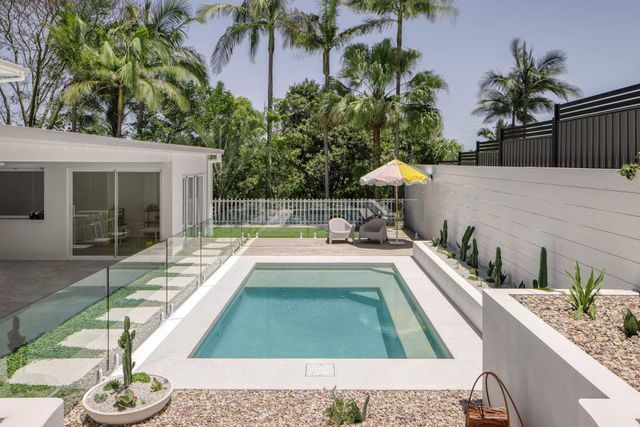 A large swimming pool is in the backyard of a house surrounded by palm trees