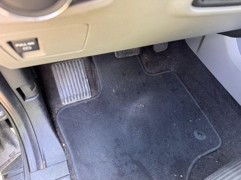The inside of a car with a black floor mat and a dashboard.