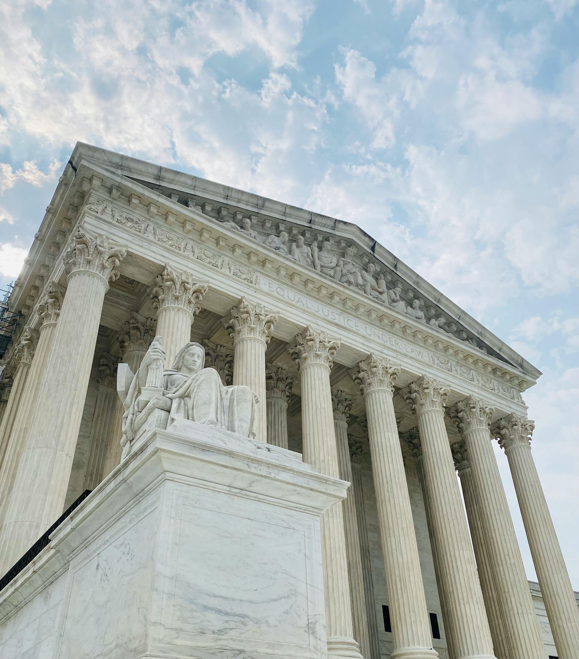 Low-angle view of the U.S. Supreme Court building’s white columns and statue against a cloudy sky