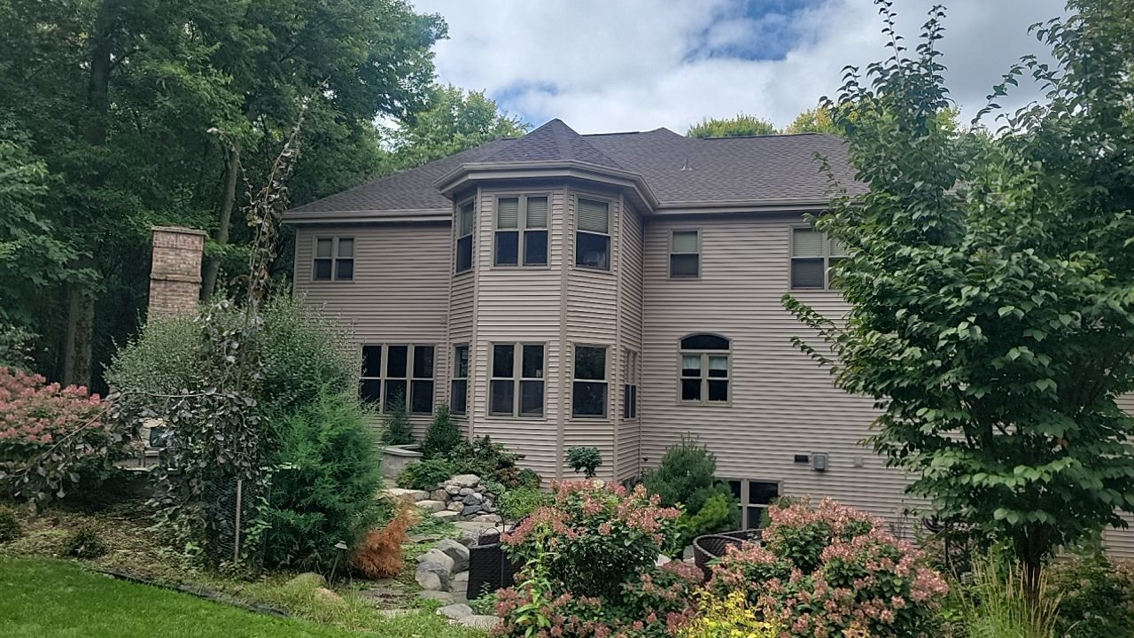 Two-story house with brick facade, white siding, black shutters, and front porch. Green lawn and blue sky.