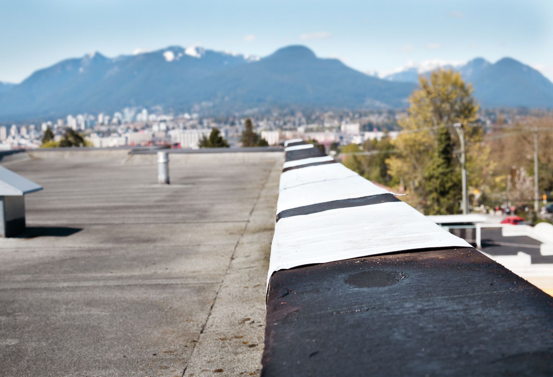 Rooftop with black and white edge, city and mountains in the background under a blue sky.