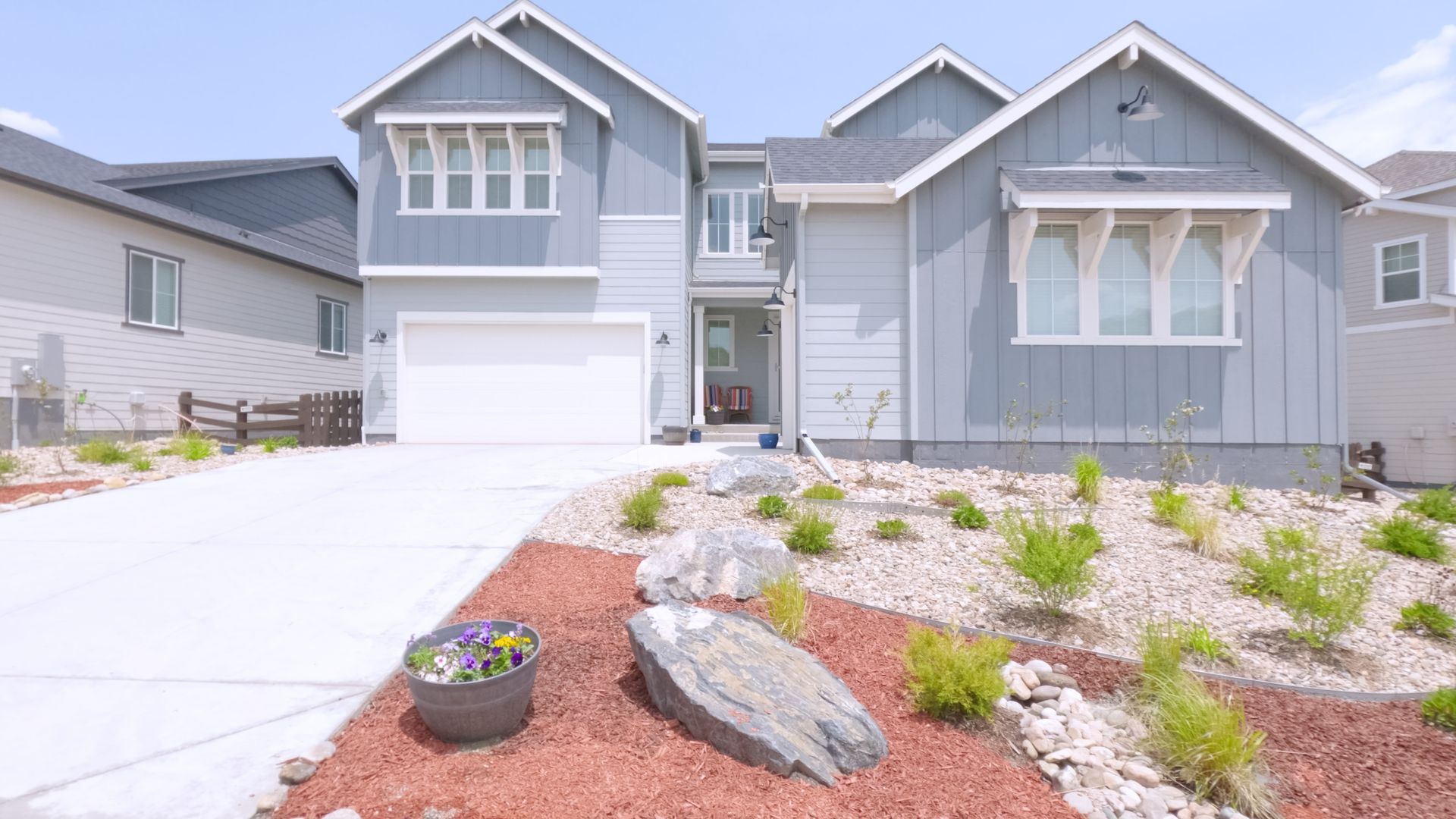 Modern gray suburban house with white trim, front garage, and landscaped rock garden under a bright sky