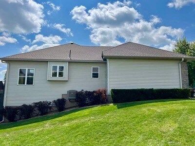A white house with a brown roof and a lot of windows is sitting on top of a lush green hill.