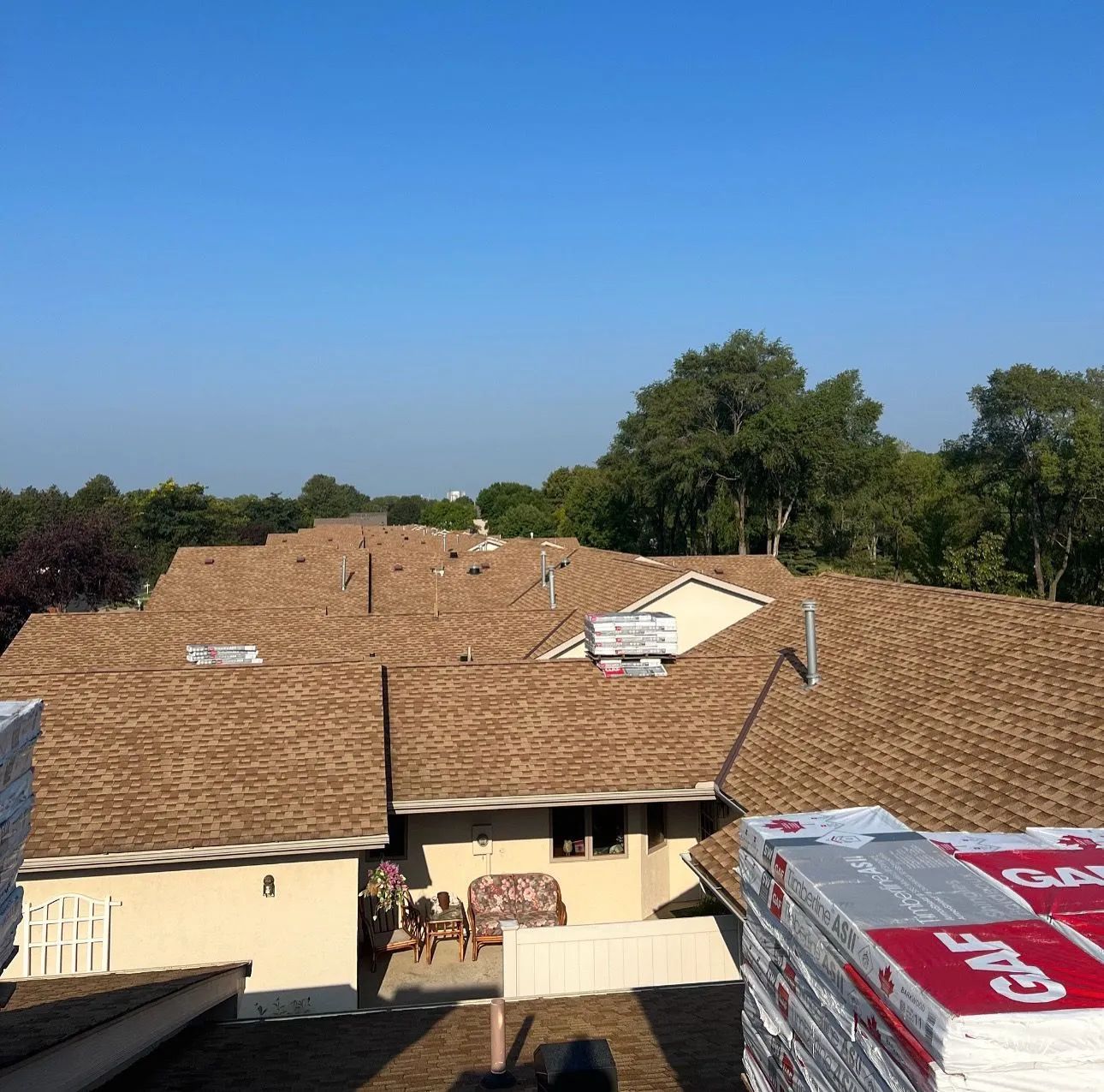 Roofs being shingled on homes; brown shingles, sunny day.