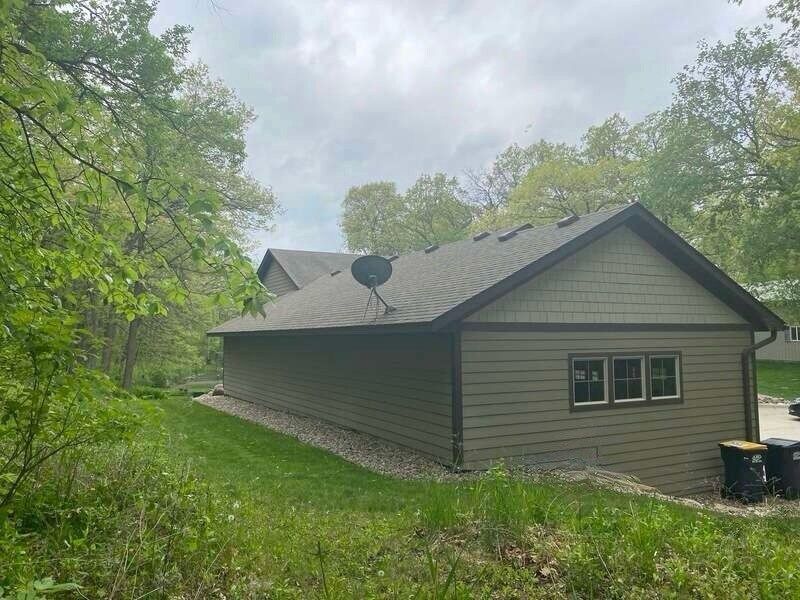A house with a satellite dish on the roof is surrounded by trees and grass.