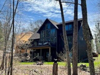 A large black house is surrounded by trees on a sunny day.