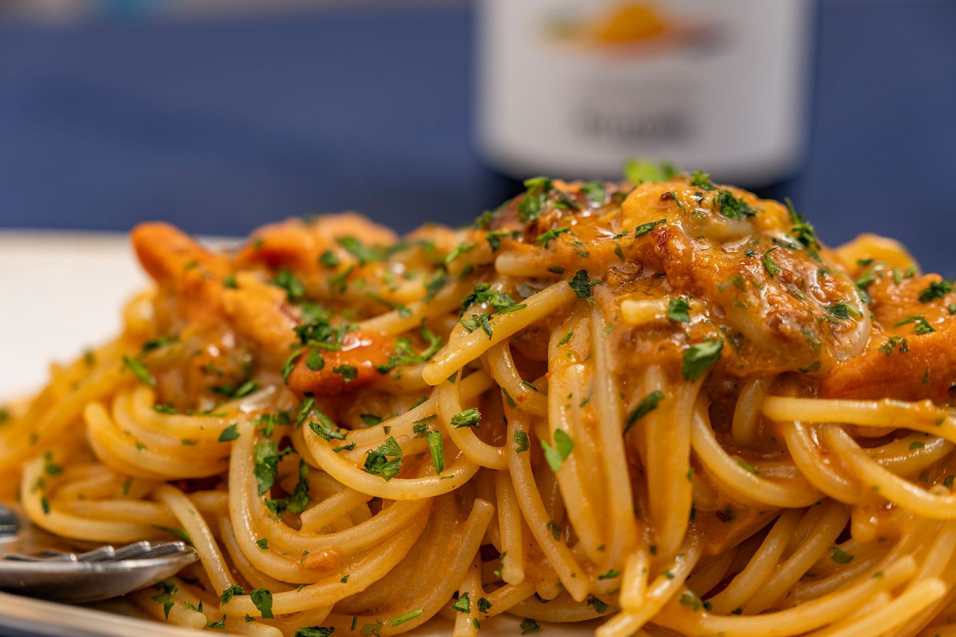 Spaghetti con salsa all'arancia e guarnizione di prezzemolo su un piatto bianco; bottiglia sfocata sullo sfondo.