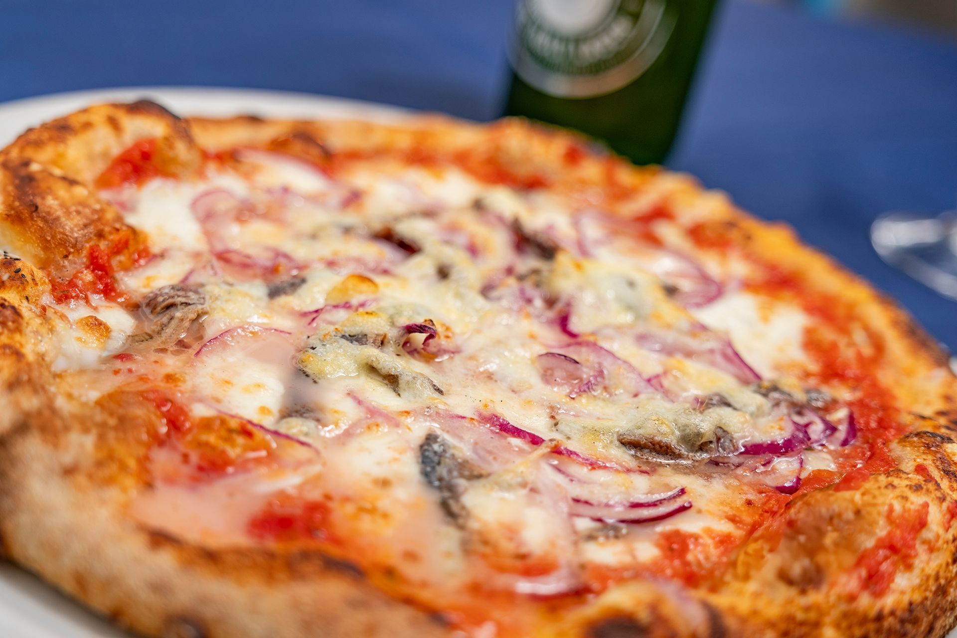 Pizza con cipolle rosse e formaggio su un piatto bianco, con una bottiglia verde sullo sfondo.