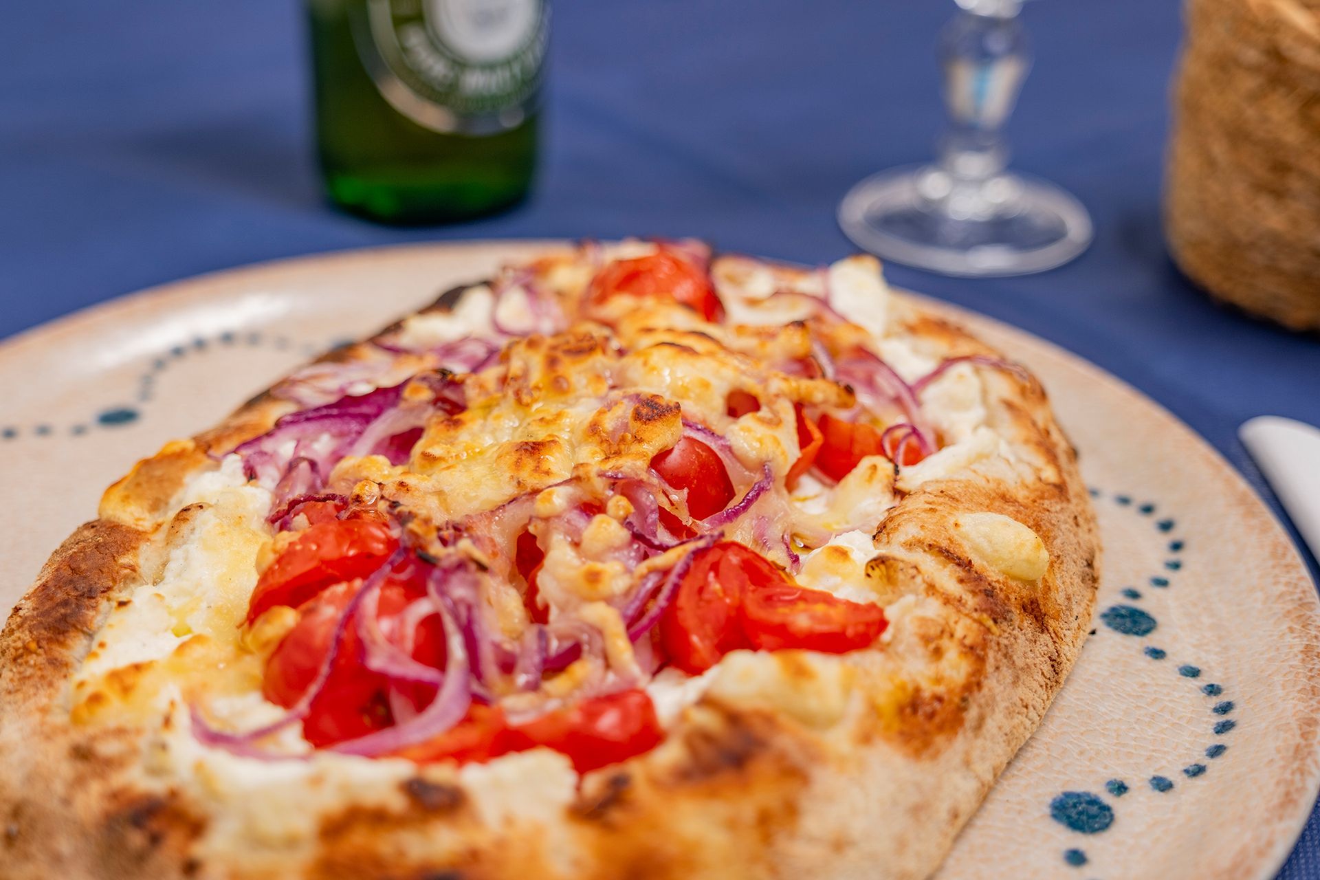 Pizza piatta condita con cipolle rosse, pomodori e formaggio su un piatto.