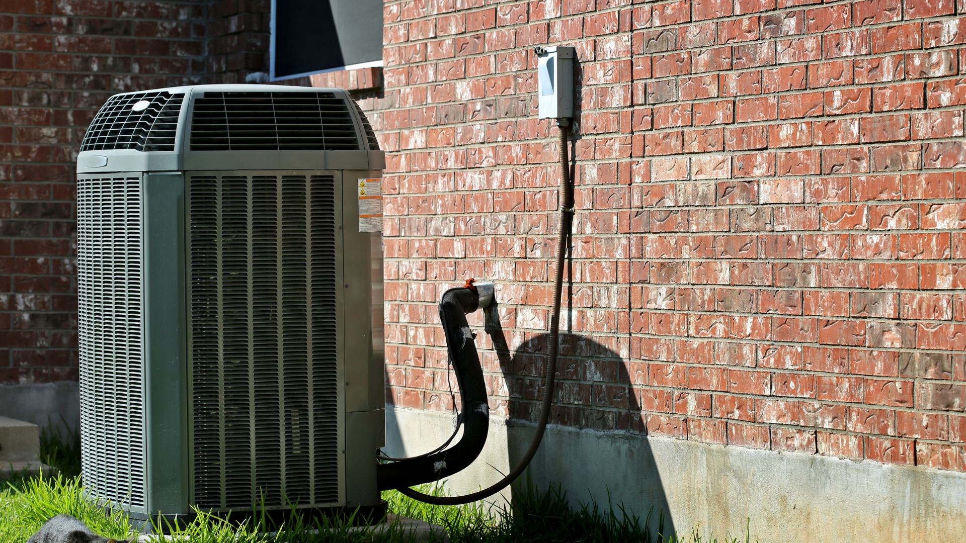 An air conditioner is sitting on the side of a brick building.