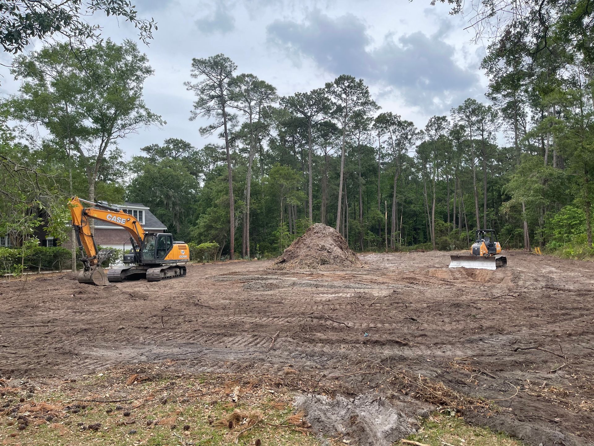 A large excavator is sitting in the middle of a dirt field surrounded by trees.