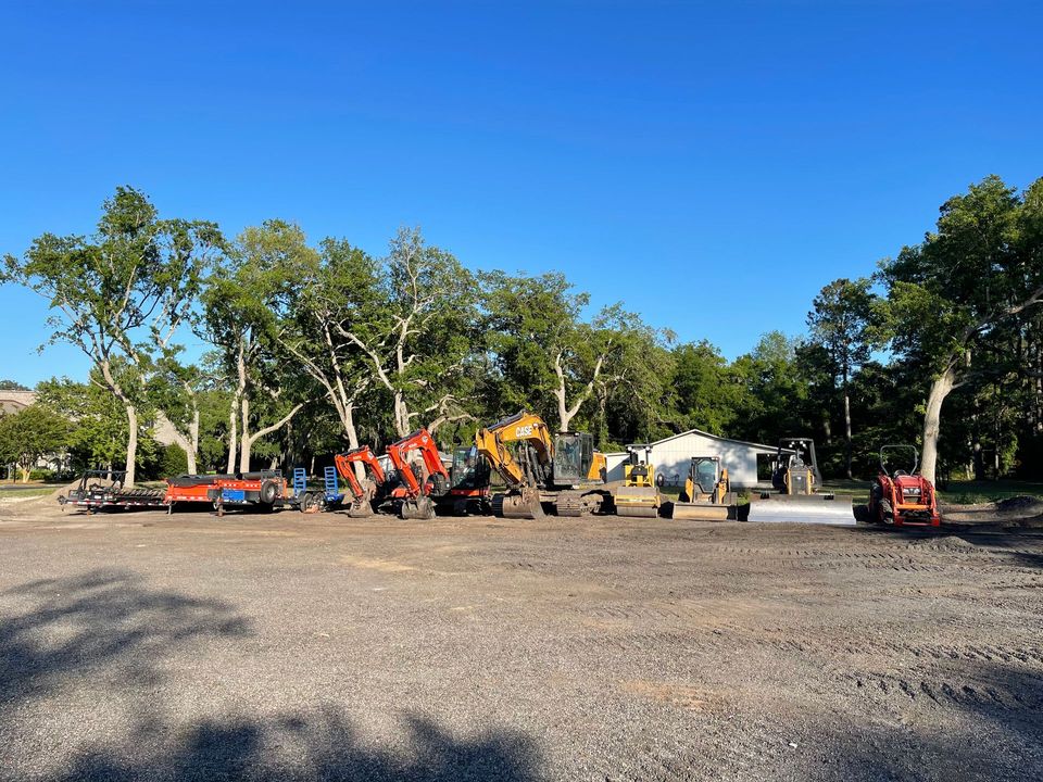 A row of construction vehicles are parked in a gravel lot.