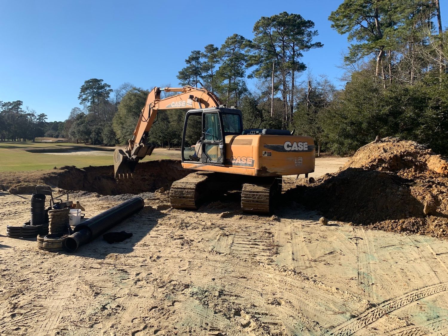 A large excavator is sitting in the middle of a dirt field surrounded by trees.