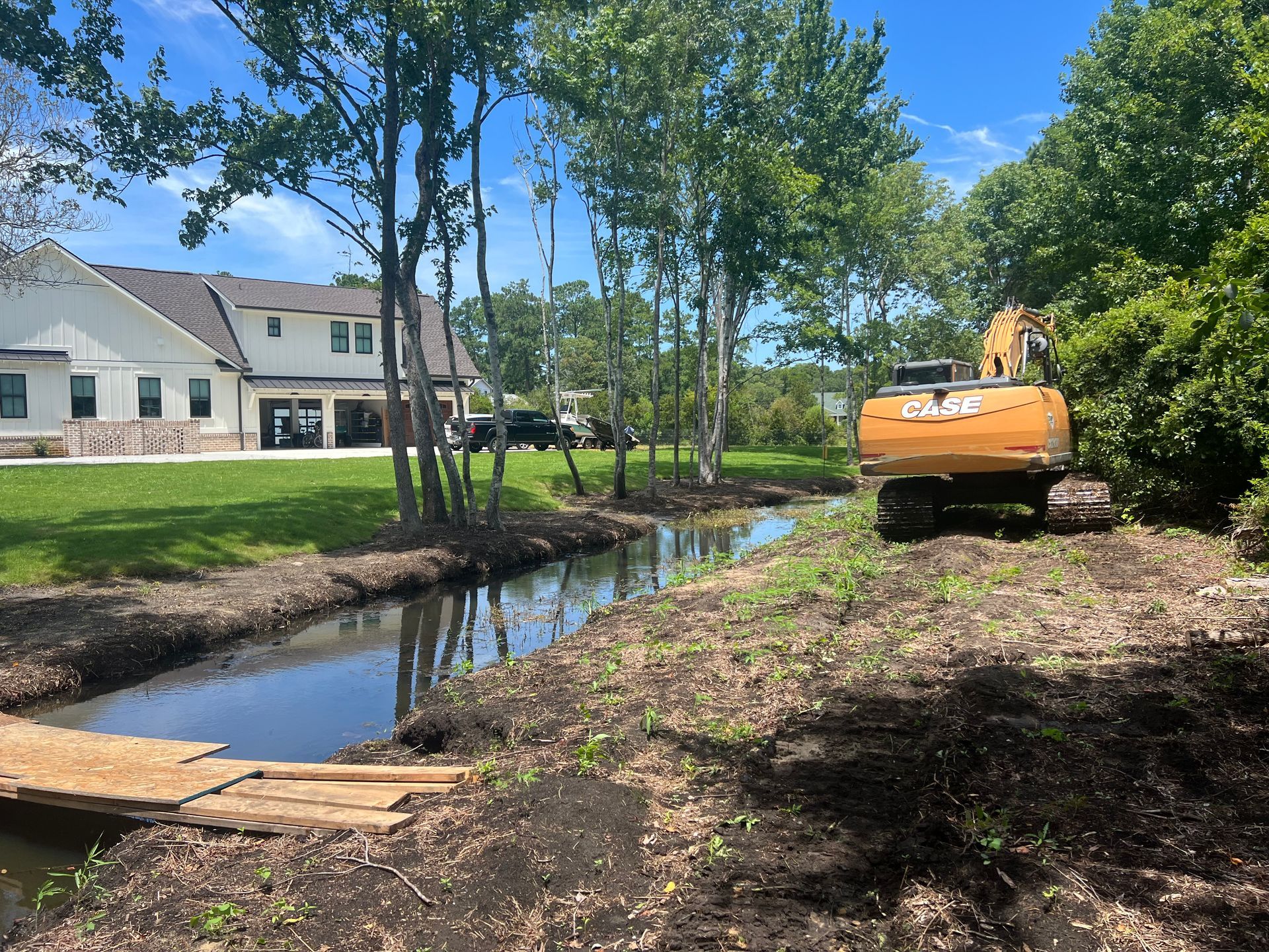 An excavator is working on a stream in front of a house.