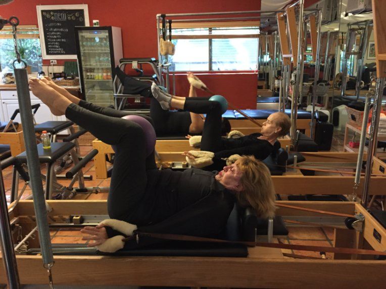 A group of people are doing pilates exercises in a studio.