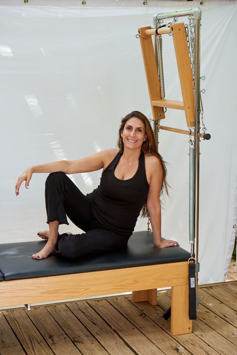 Maria is sitting on a wooden pilates machine .