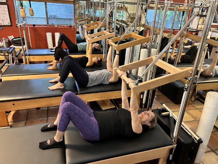 A group of people are doing pilates exercises in a studio.