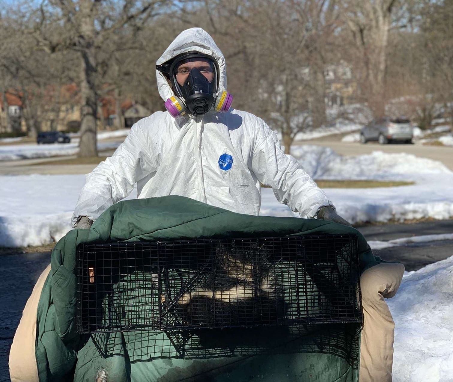 A man wearing a gas mask is holding a cat in a cage.