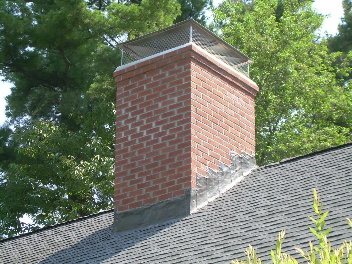 A brick chimney on top of a roof with trees in the background