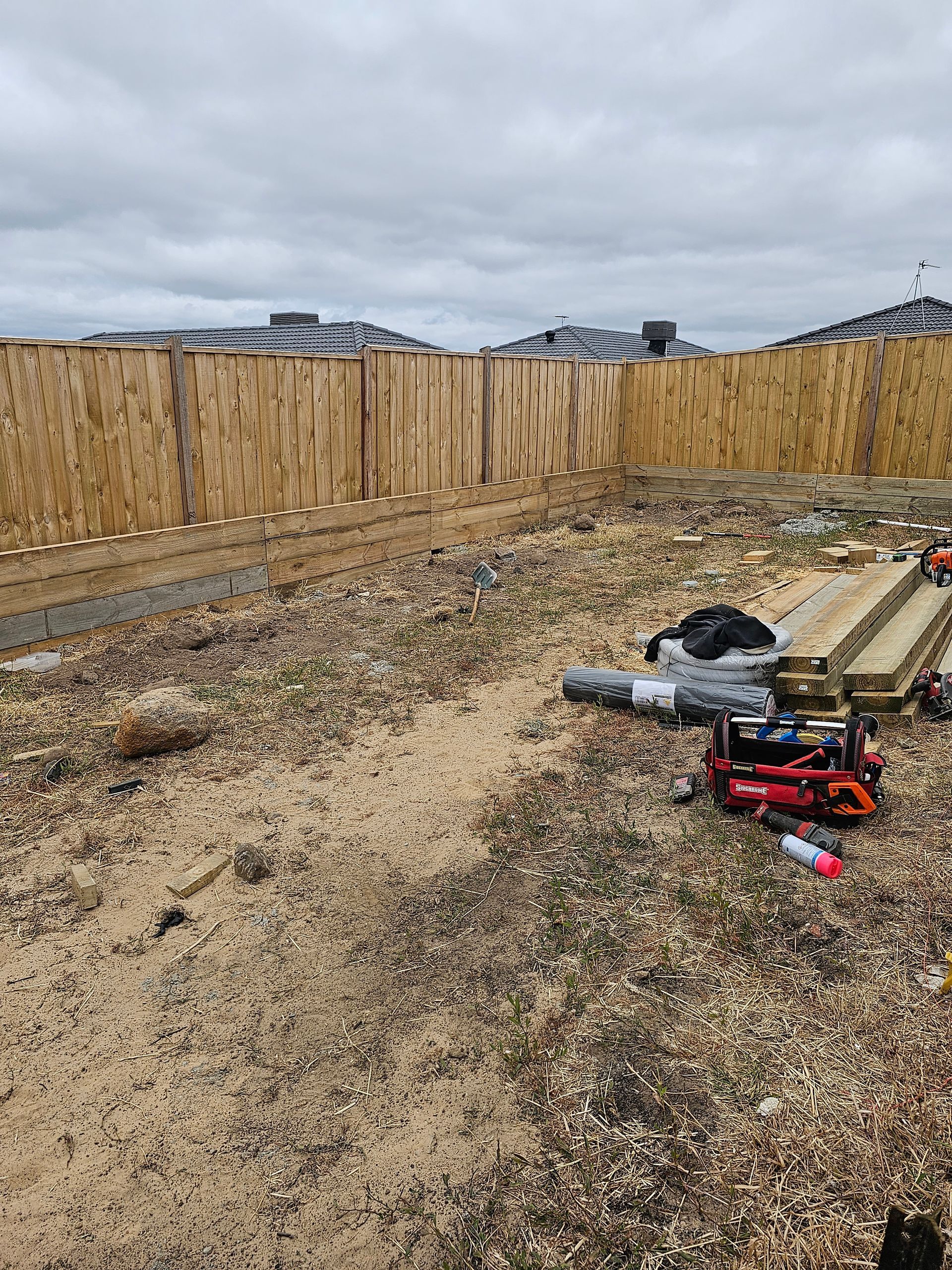 Construction site with wooden fence, wood scraps, tools, and overcast sky.