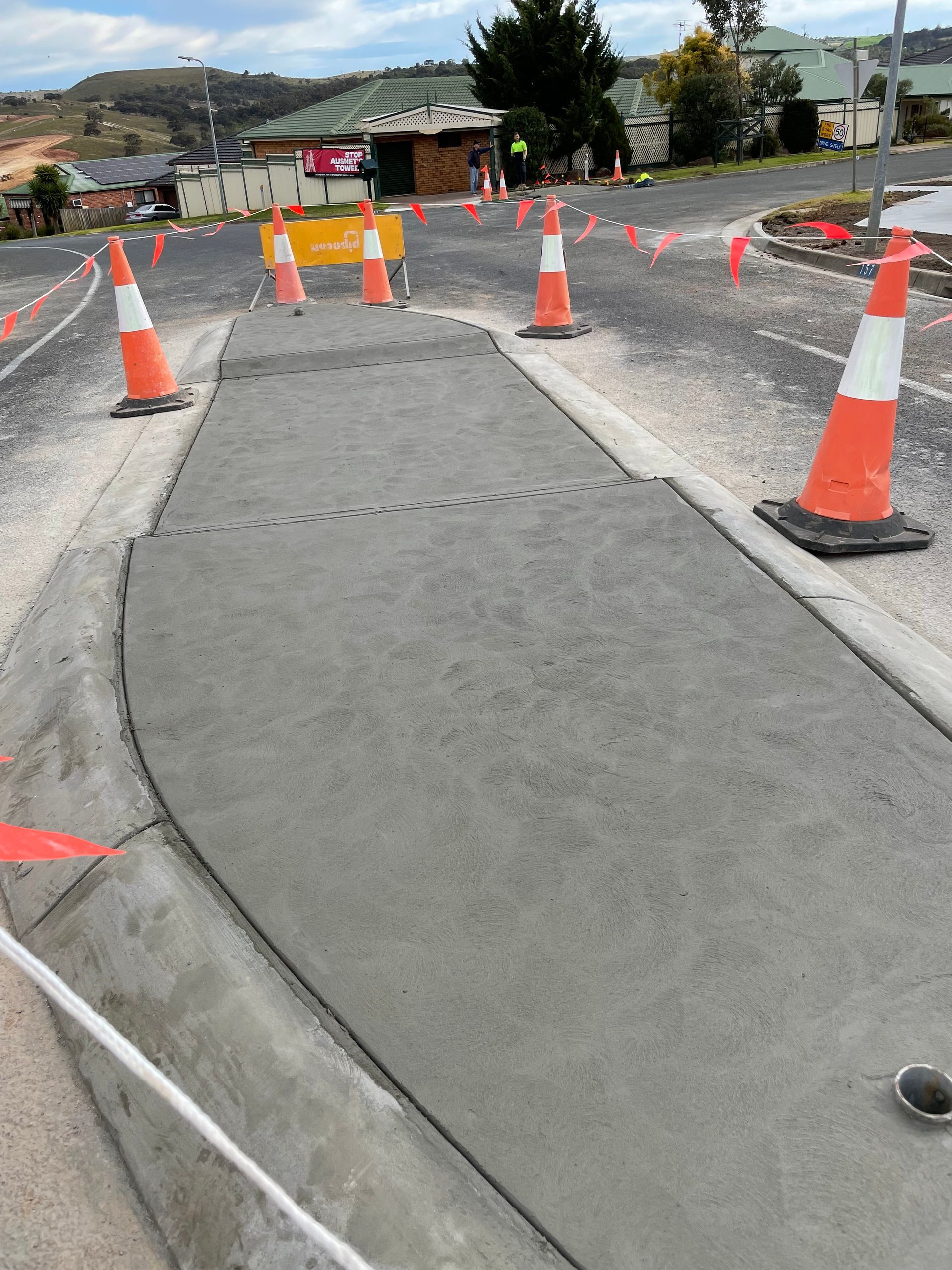 Freshly poured concrete section of a road with orange traffic cones. Road work in progress.