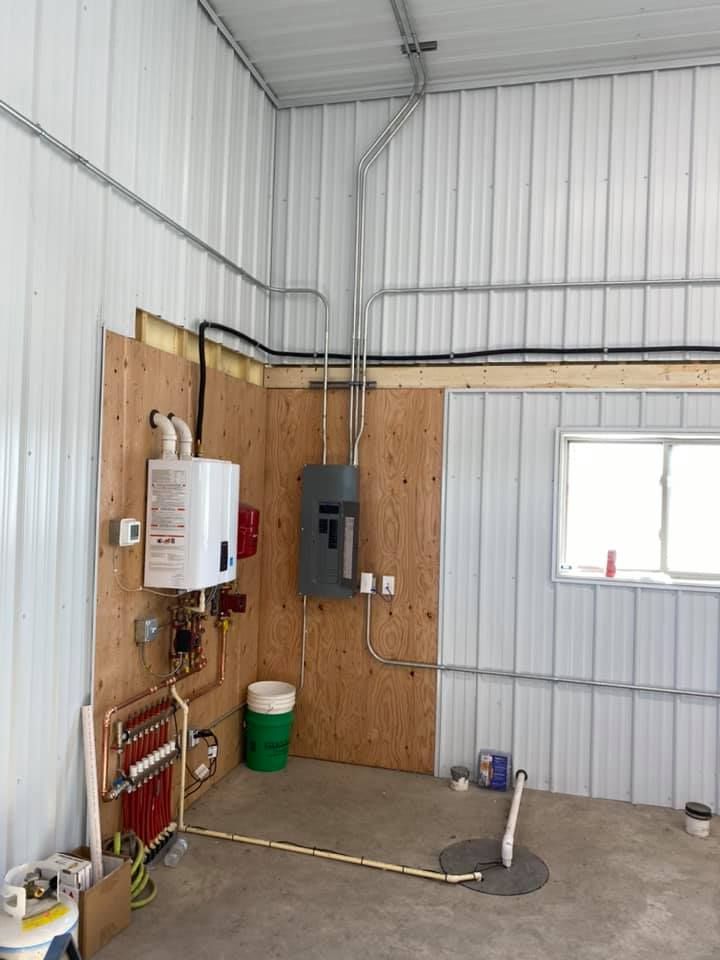 Water heater and related plumbing in a metal-walled building. Plumbing pipes run along the wall.