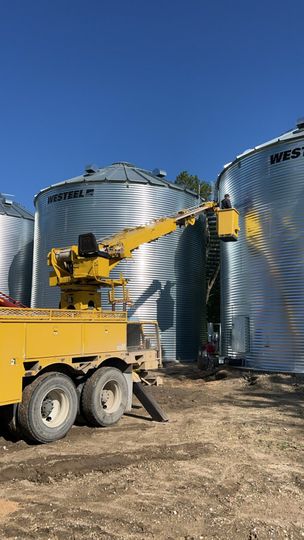 Yellow crane near large metal grain silos on a sunny day.