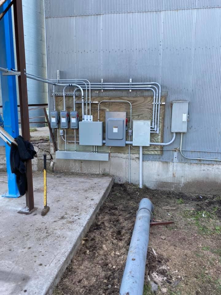 Electrical boxes and conduits on a corrugated metal building. Conduit runs horizontally, dirt trench in foreground.