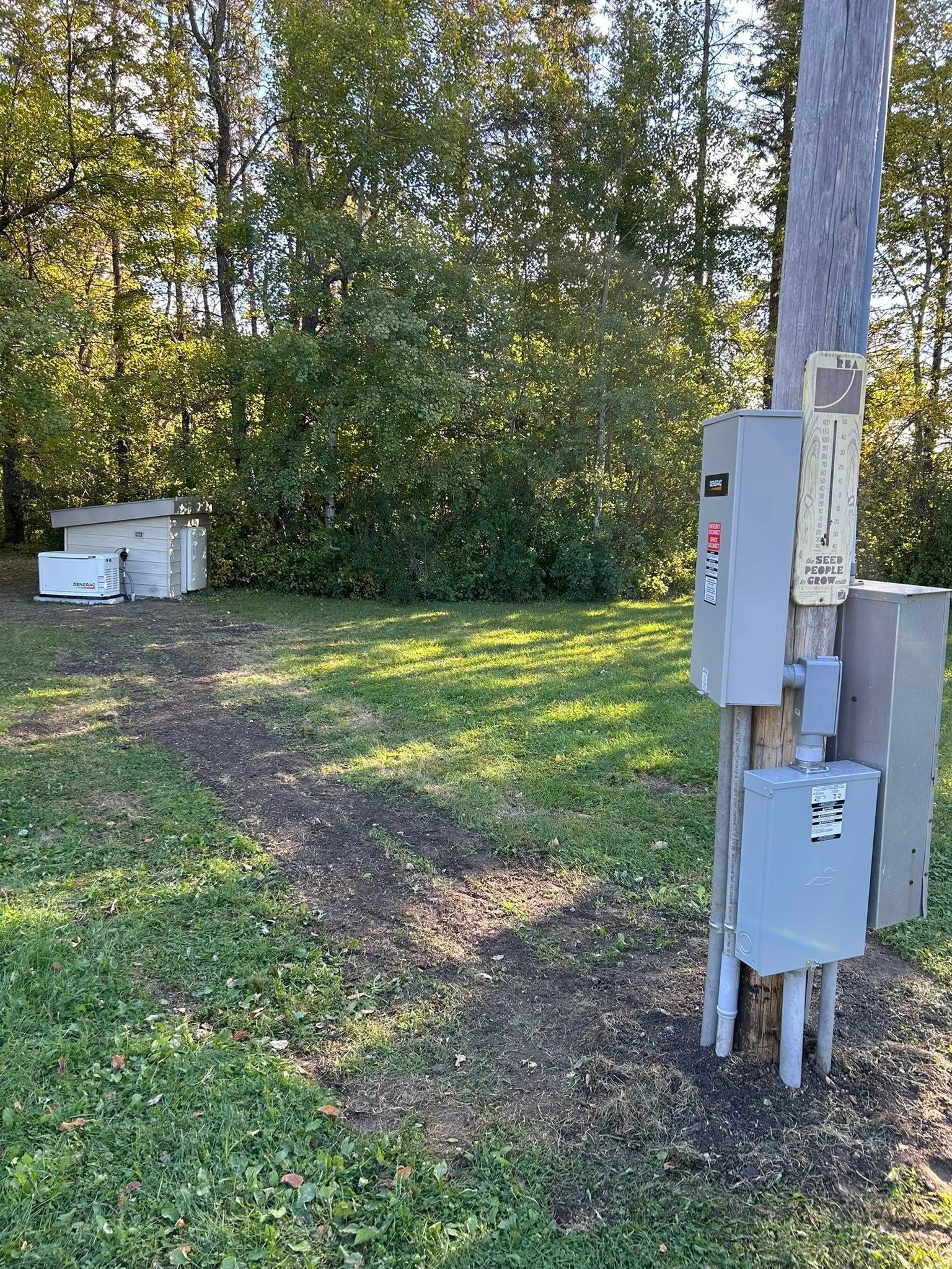 Electrical boxes on a utility pole next to a grassy path and forest background.