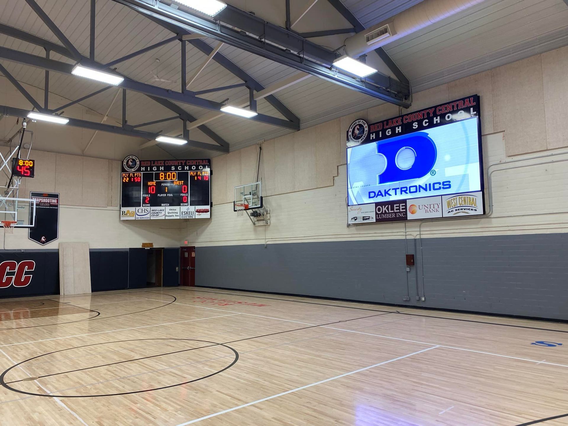 Basketball court with scoreboards and large video screen, showing logo. Empty wood floor and padded wall.