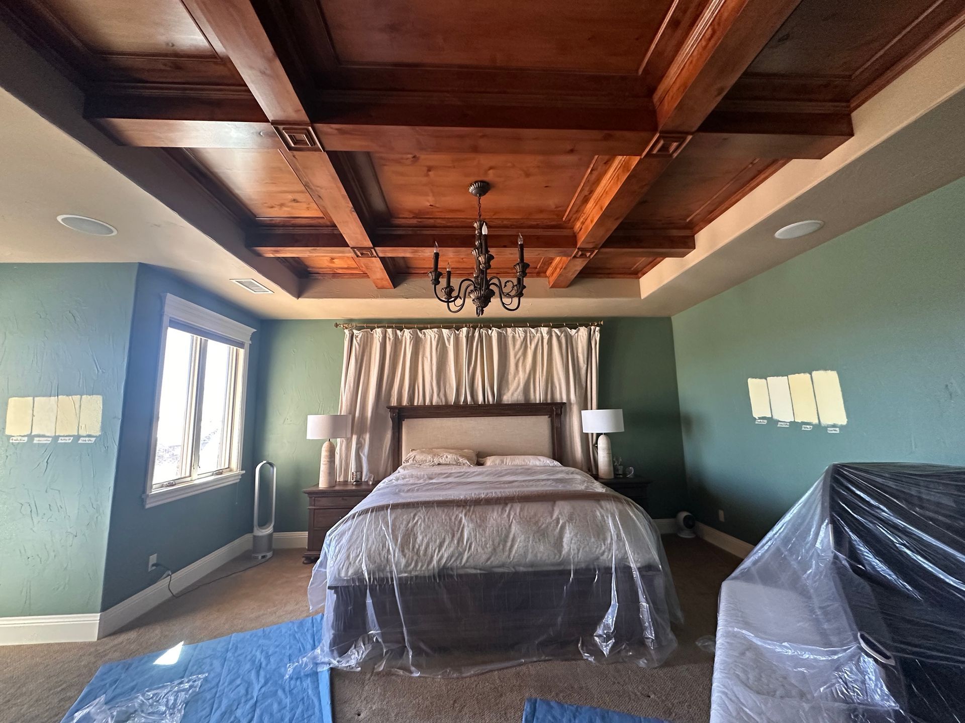Bedroom with green walls, wooden ceiling beams, bed, and chandelier.